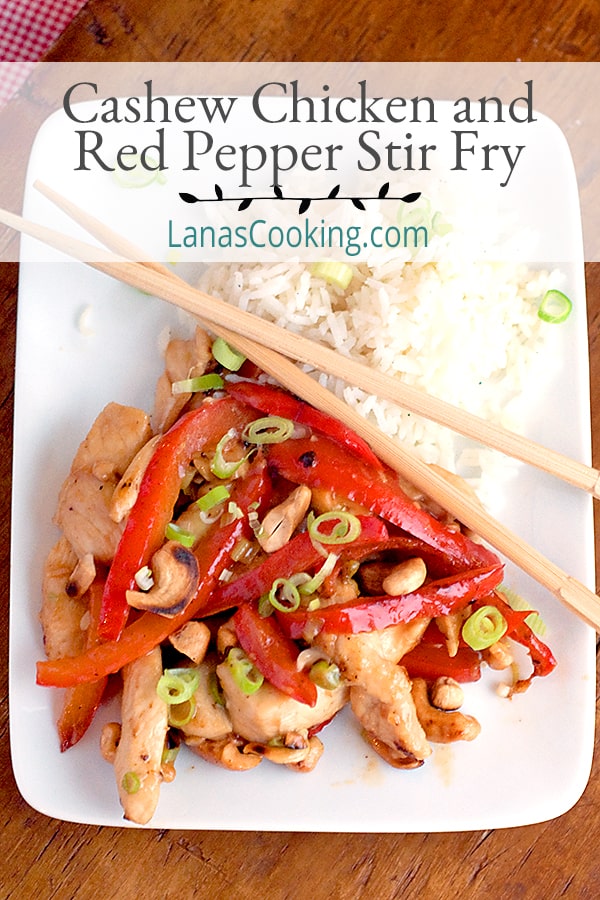 Cashew chicken and red pepper stir fry with rice and green onion garnish on a white plate.