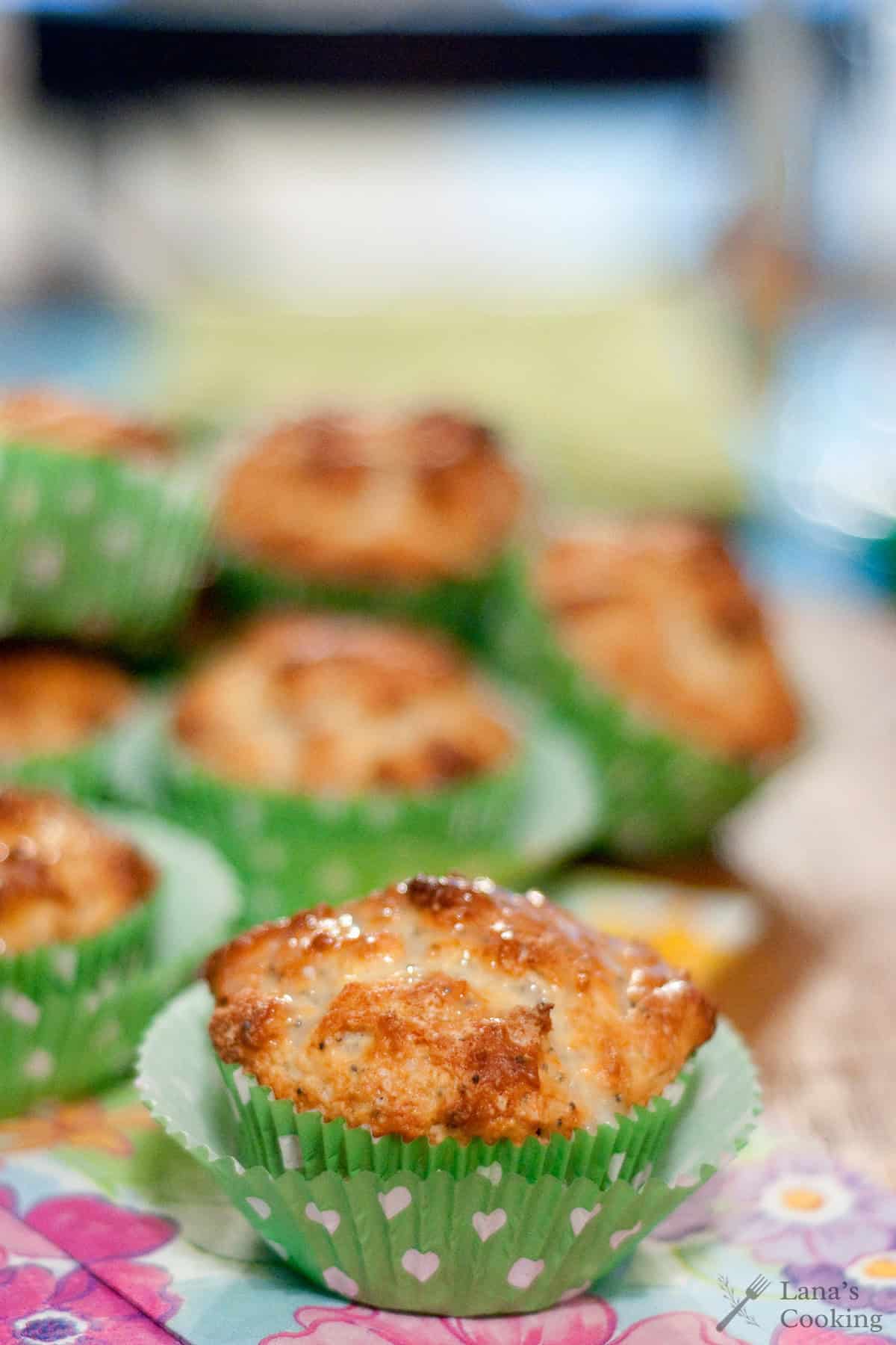 A close-up of freshly baked muffins in green cupcake wrappers with white hearts, arranged on a colorful floral napkin.
