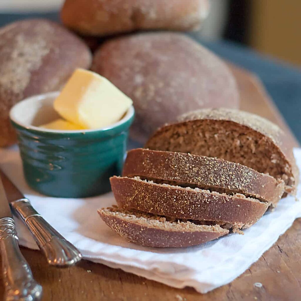 Steakhouse honey wheat bread sliced on a serving board with a napkin and a container of butter.