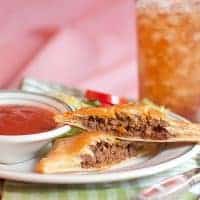 Two Italian style hand pies on a plate with a small dish of marinara dipping sauce.