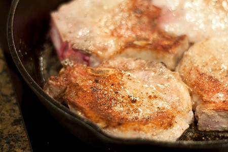 Browning pork chops on the second side in a skillet.