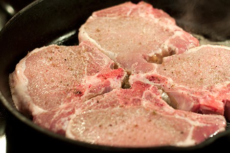 Pork chops seasoned and in the skillet.