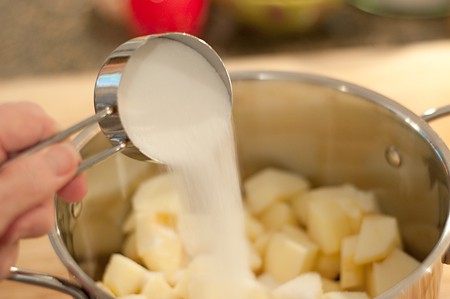 Adding sugar to apple pieces in a saucepan.