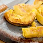 Baked Acorn Squash on a baking sheet with a chef's knife in the background.