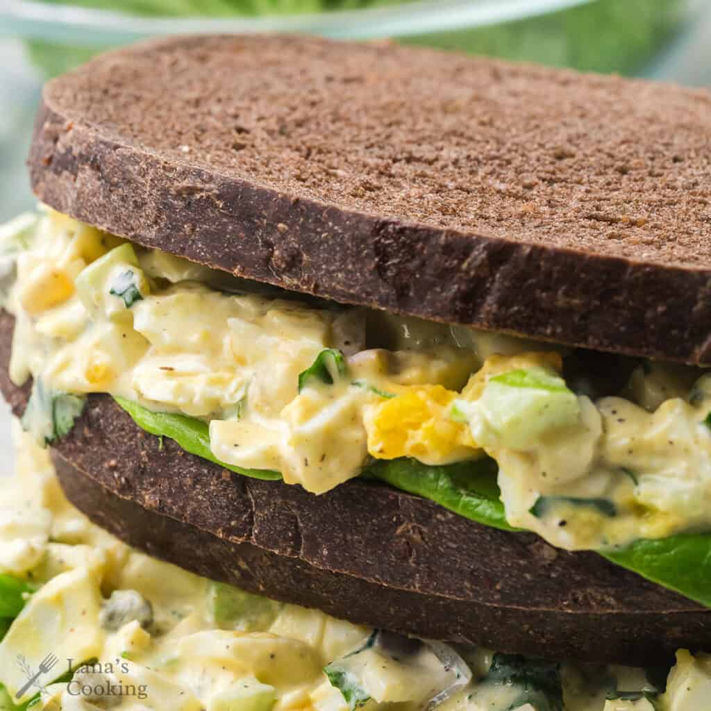 Two finished herbed egg salad sandwiches presented in a stack.
