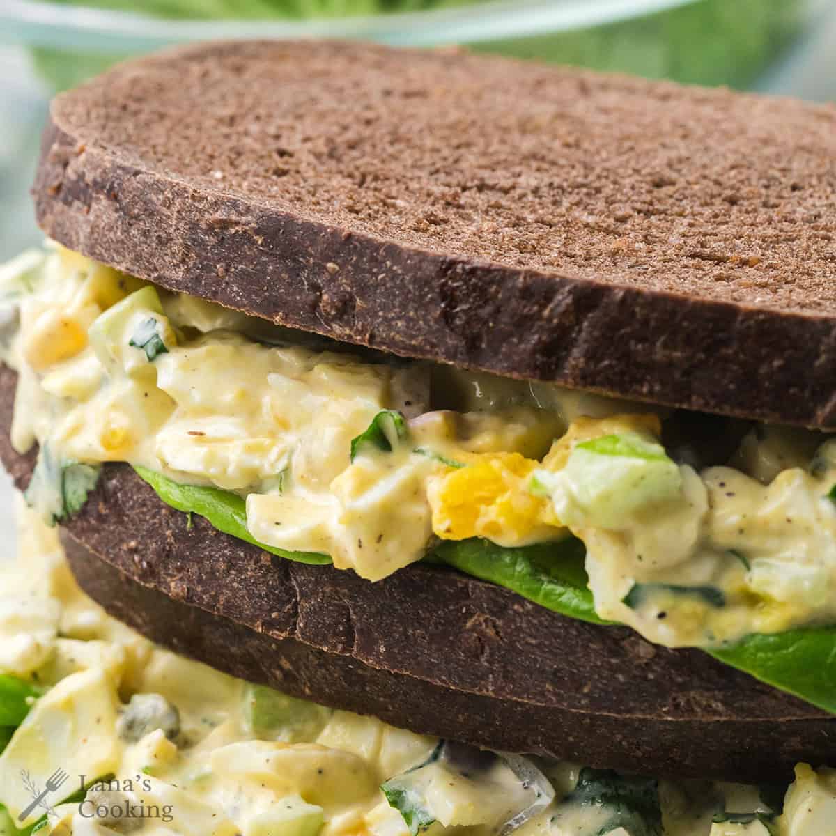 Two finished herbed egg salad sandwiches presented in a stack.