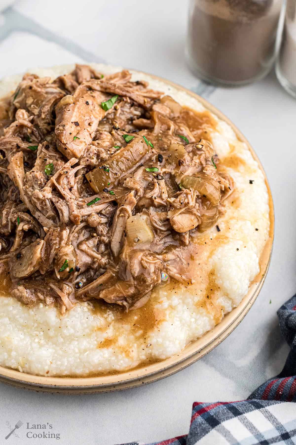 Pork ragu over buttered grits on a dinner plate.