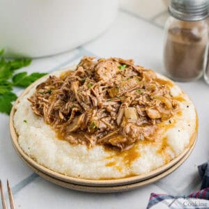 Pork ragu over buttered grits on a dinner plate.