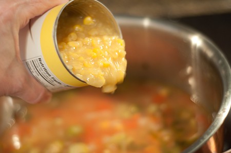 Adding creamed corn to the soup pot.