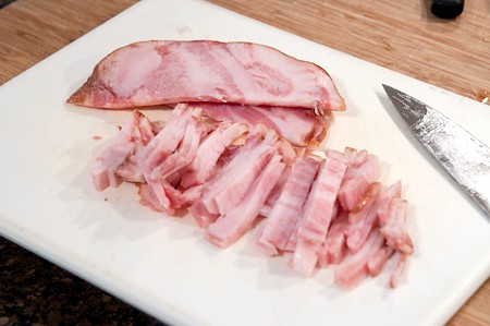 Slicing pig jowls (guanciale) on a cutting board.