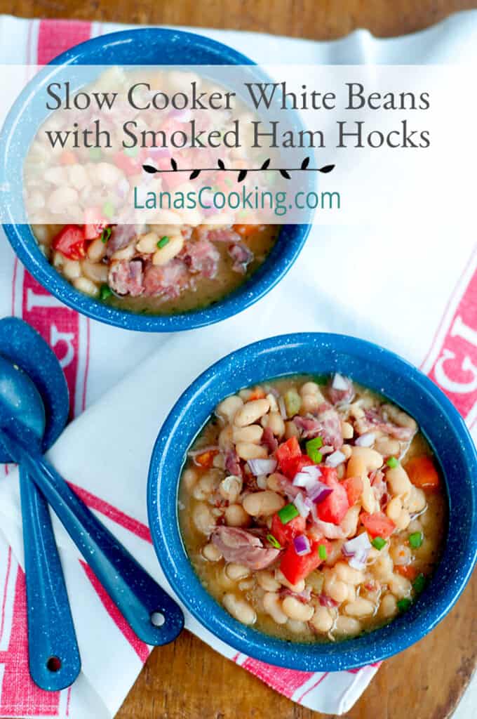 Two bowls of Slow Cooker White Beans with Smoked Ham Hocks presented on a wooden board with a kitchen towel and spoons. Text overlay for pinning.