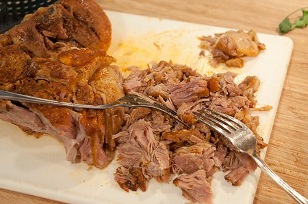 Using forks to pull the pork meat into shreds.