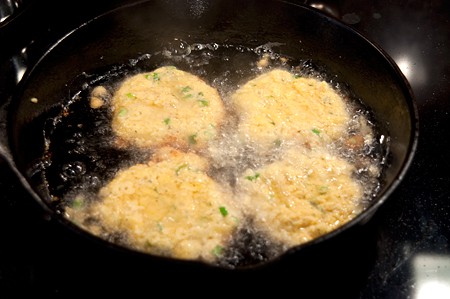 Fritters cooking in hot oil in a cast iron skillet.