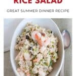 Oval bowl of shrimp and rice salad with veggies, beside a spoon on a neutral placemat.
