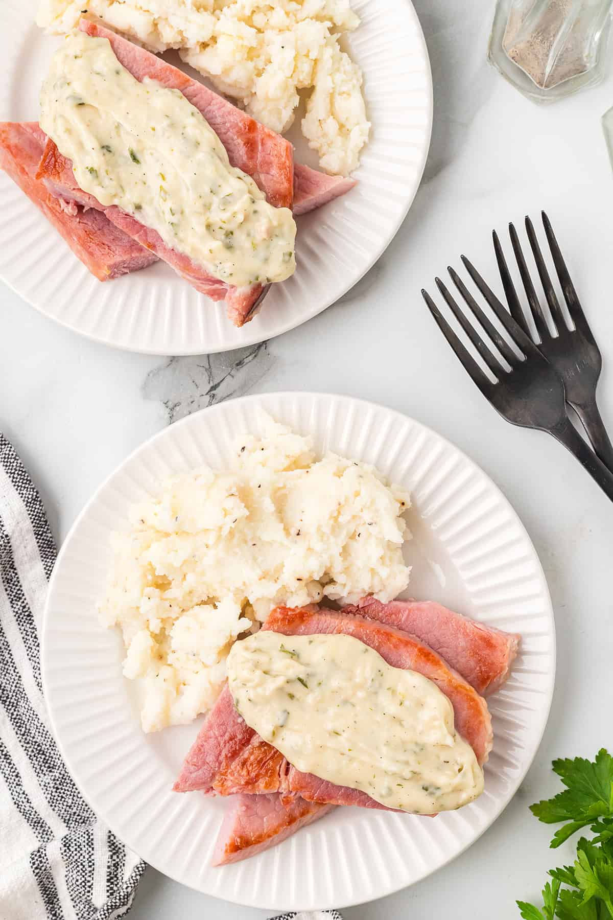 A slice of ham topped with creamy sauce on a white dinner plate.