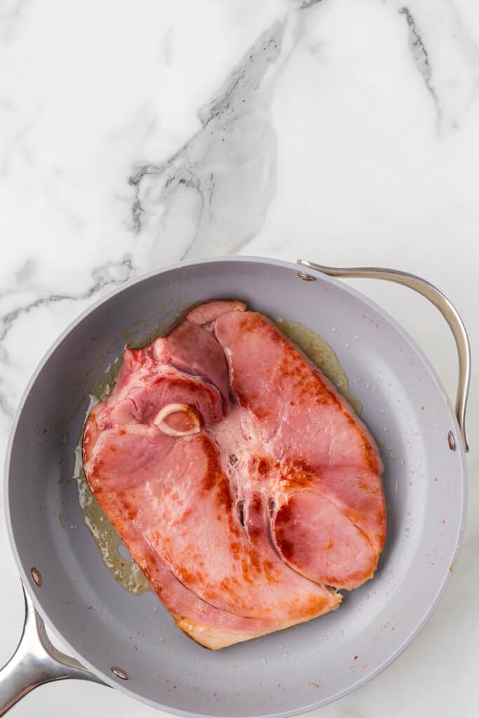 A browned ham steak in a frying pan.