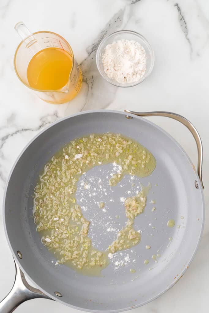 Flour sprinkled over cooked shallots in a skillet.