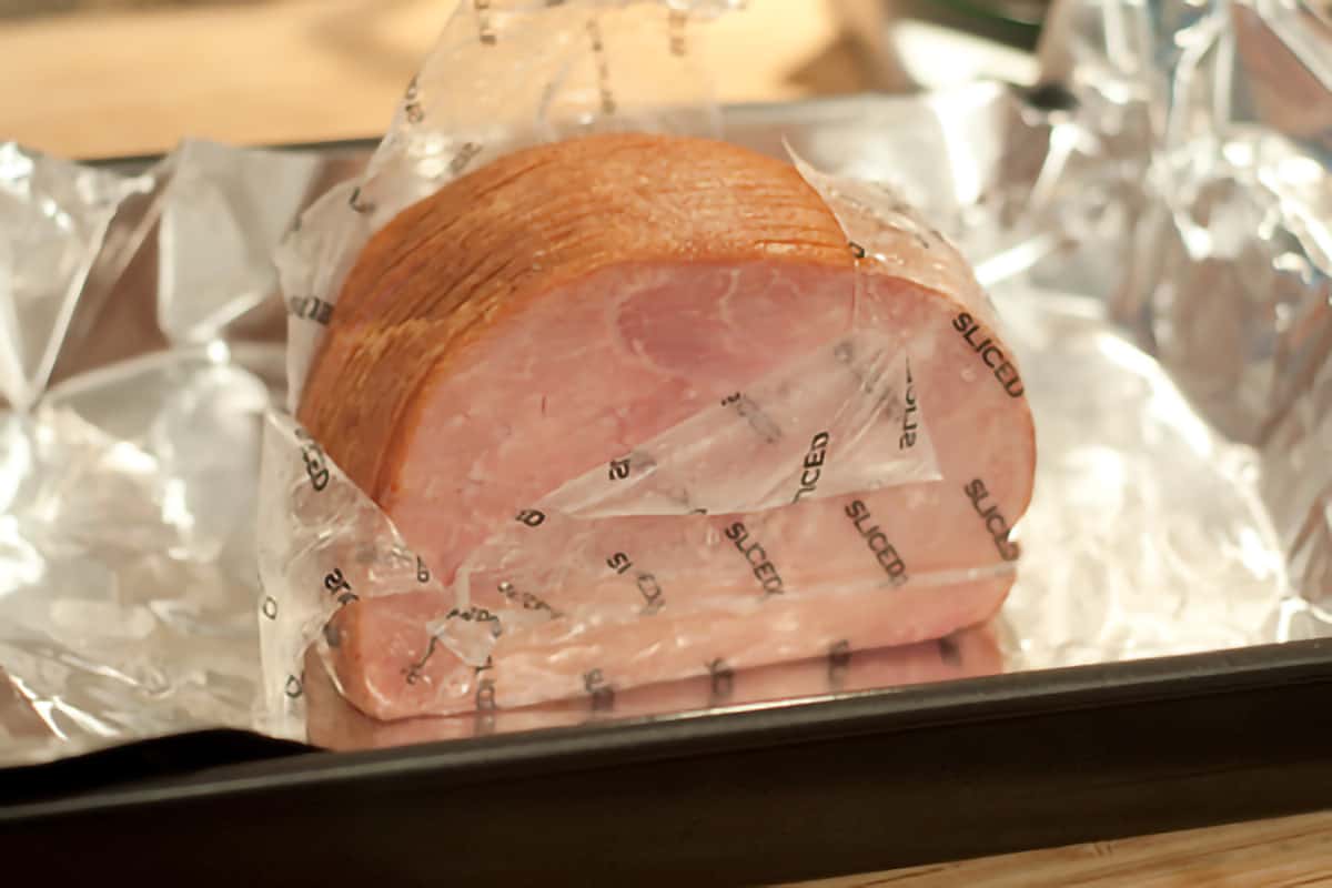 Smithfield boneless ham being prepared for cooking; the ham is partially opened and sitting on aluminum foil in a baking pan.
