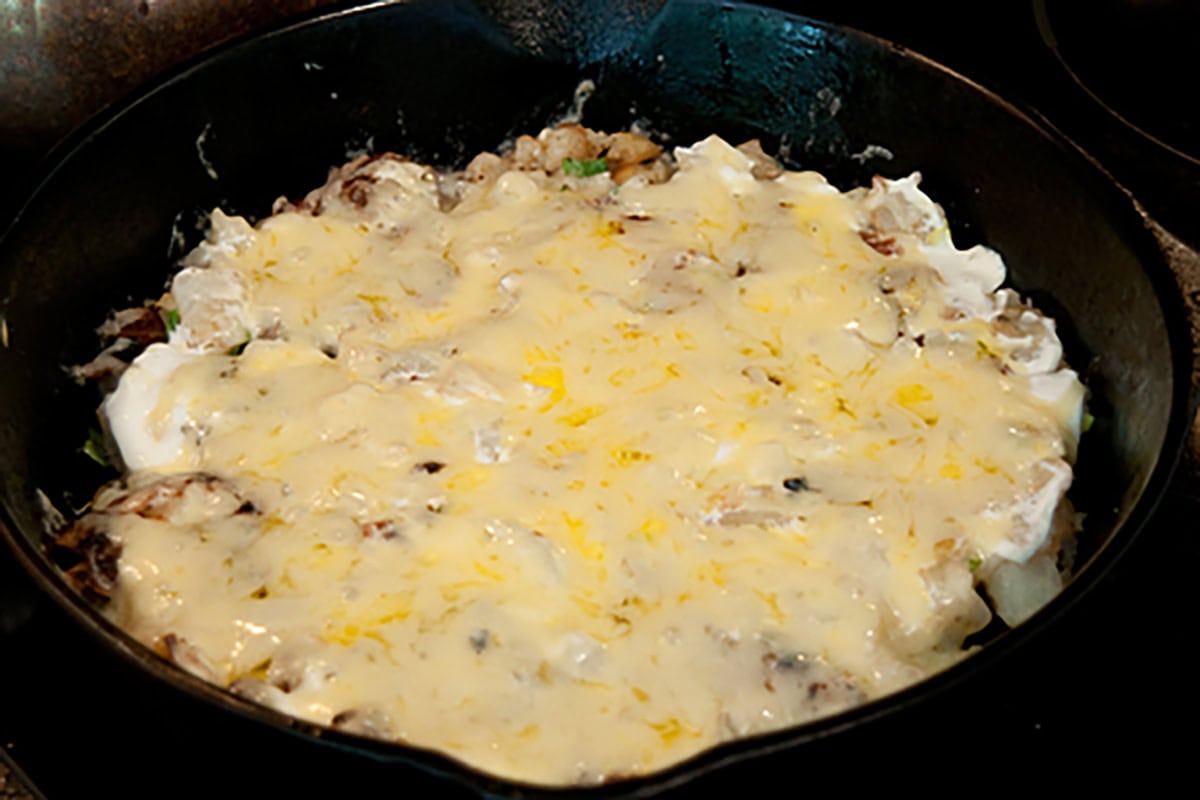A skillet filled with a melted cheese and vegetable mixture, cooked and lightly browned on top.