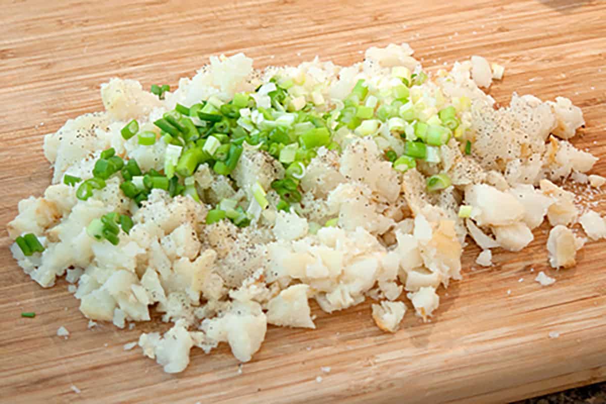 Chopped potatoes and diced green onions with black pepper on a wooden cutting board.