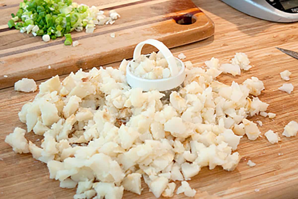 Chopped baked potatoes on a cutting board with diced green onions in the background.