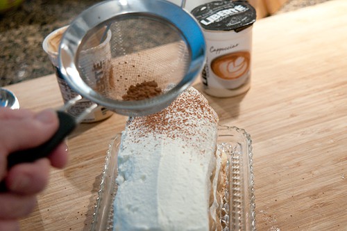 Sprinkling powdered cocoa over assembled tiramisu.