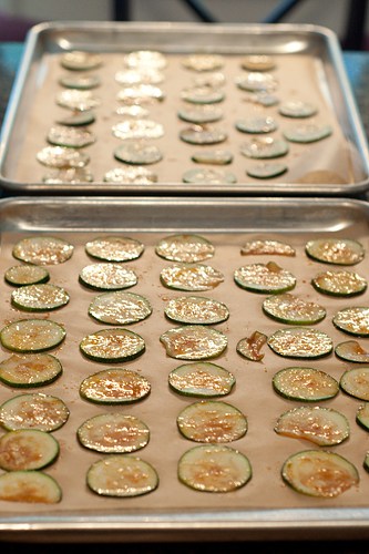 Two baking sheets lined with parchment and zucchini chips ready to bake.