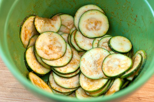 Zucchini slices coated with oil and spices in a green bowl.