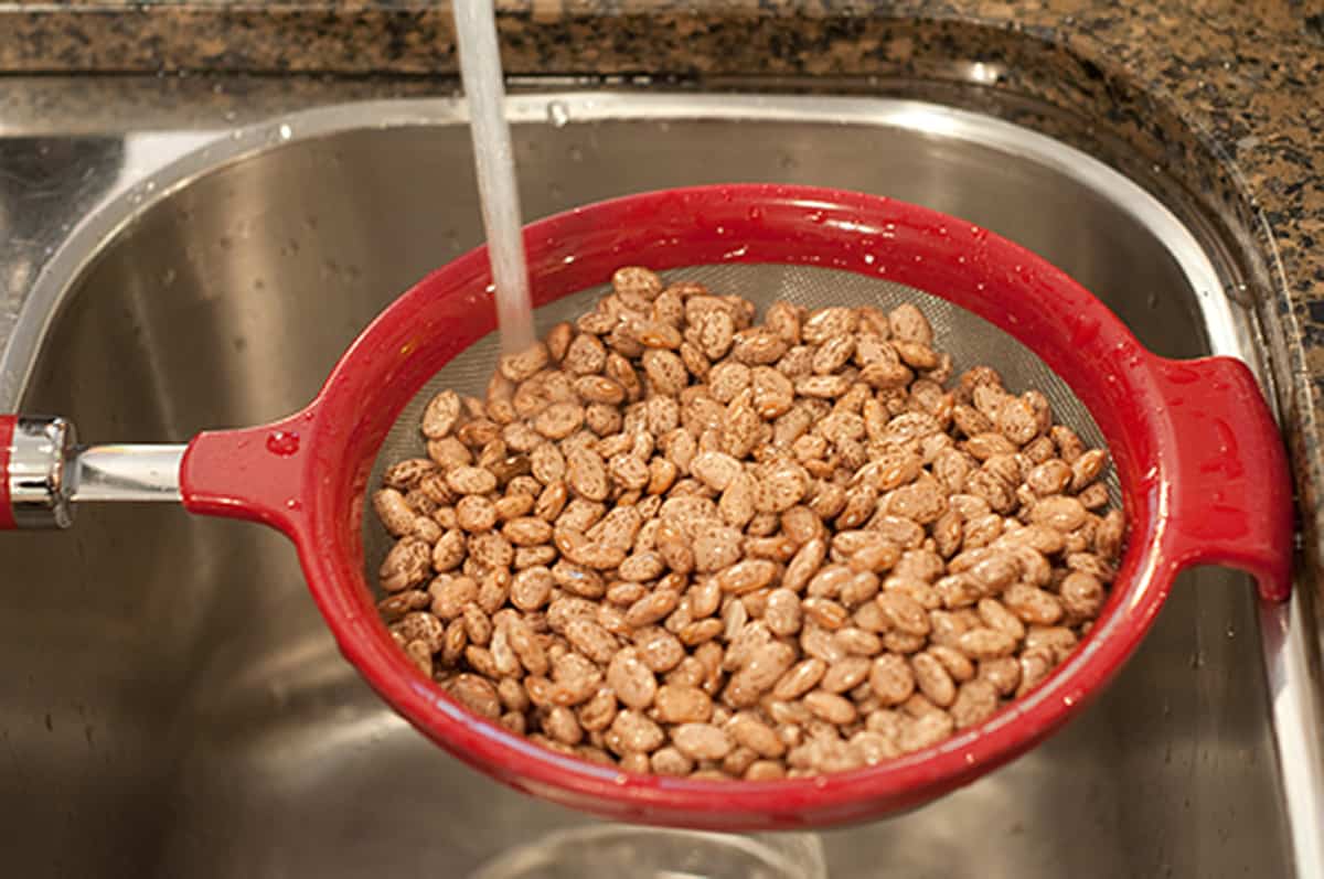 Rinsing dried pinto beans under the sink tap.