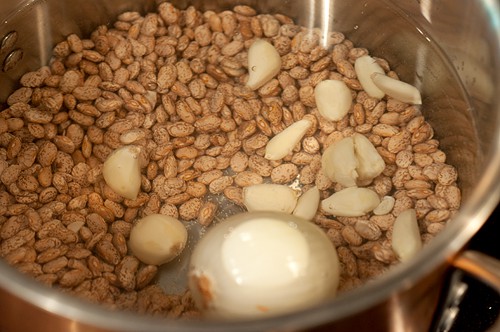 Pinto beans in a pot with water, onion, and garlic.