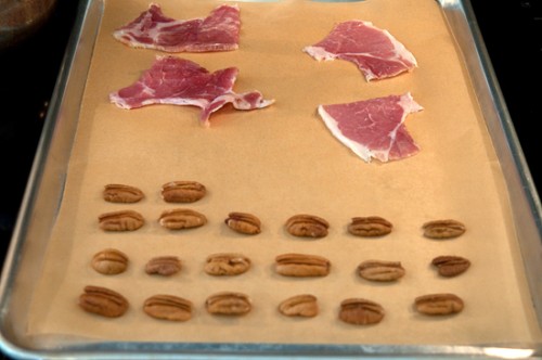Slices of country ham and pecan halves on a baking sheet lined with parchment paper.