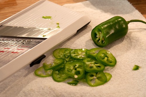 Jalapeno slices on a paper towel beside a mandolin.
