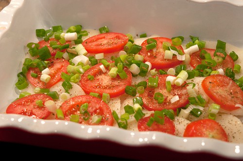 Potato and tomato slices topped with green onions in a baking dish.
