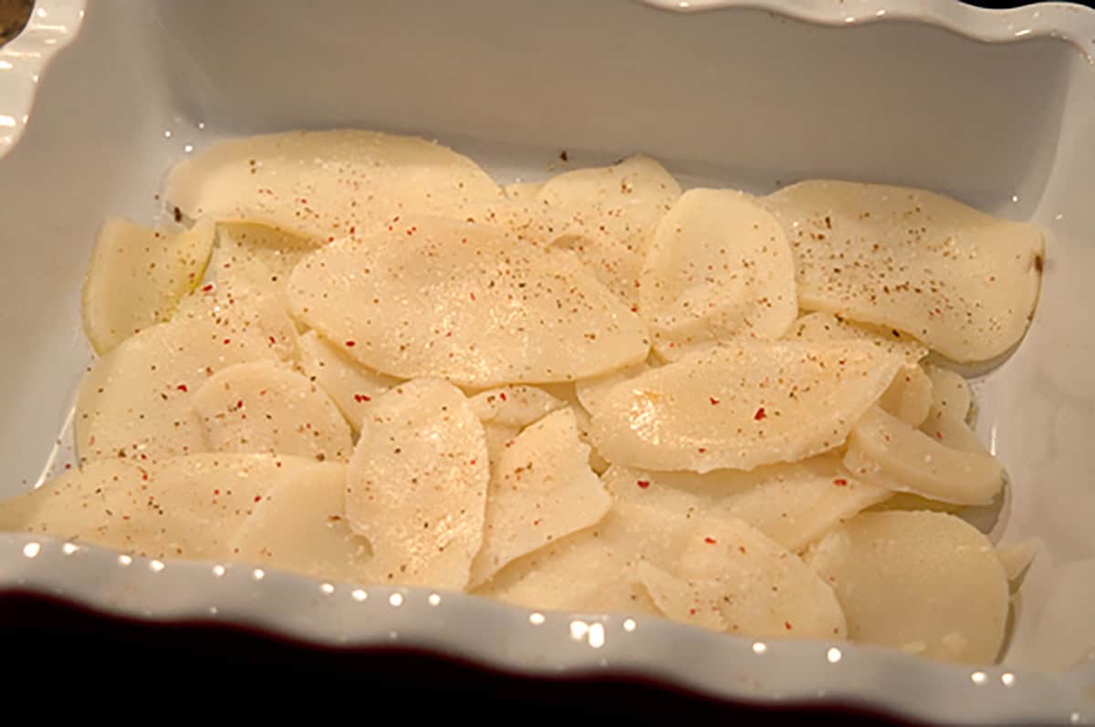 Potato slices added to the baking dish and sprinkled with salt and pepper.