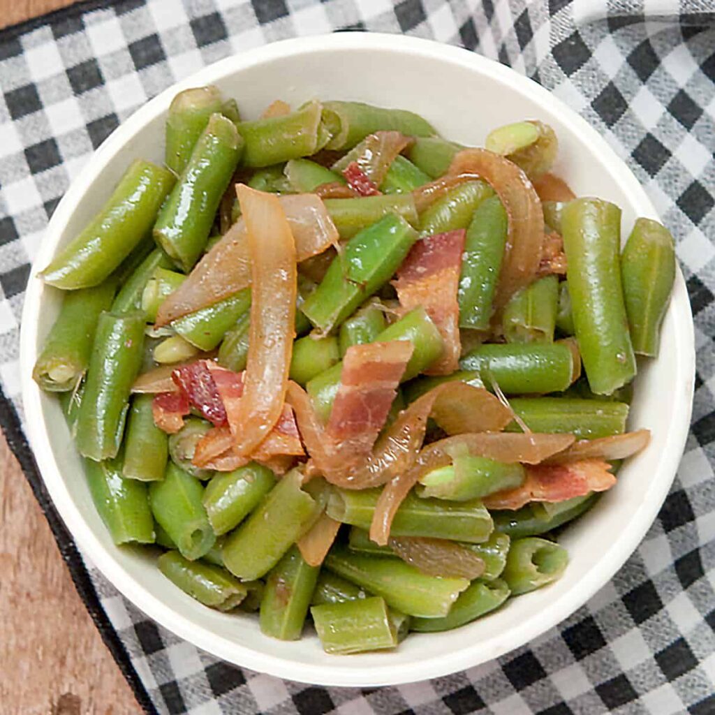 Green beans in a white bowl on a black and white checked napkin.