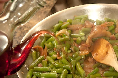 Adding red wine vinegar to the skillet with green beans, onions, and bacon.