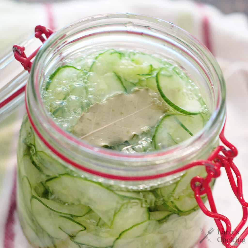 Glass jar filled with quick pickled cucumbers, tangy pickling liquid, and a bay leaf, resting on a white towel with red stripes.