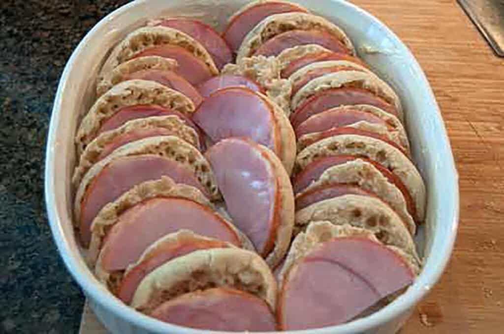 English muffins and ham layered in a casserole dish.