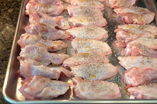 Wing pieces arranged on a baking sheet and sprinkled with salt and pepper.