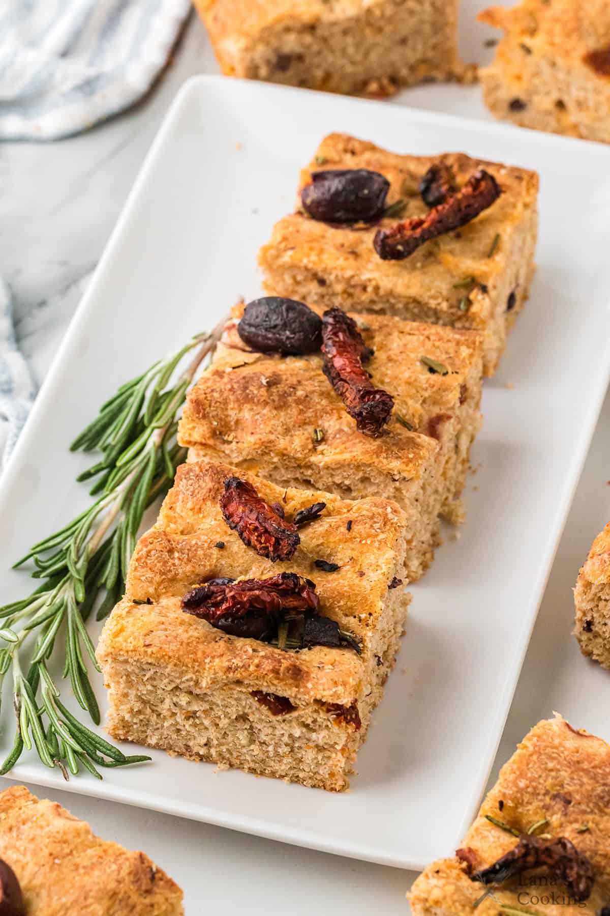 Three slices of focaccia bread topped with olives and sun-dried tomatoes, garnished with fresh rosemary.