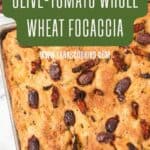 Golden focaccia bread topped with kalamata olives and sun-dried tomatoes on a baking tray.