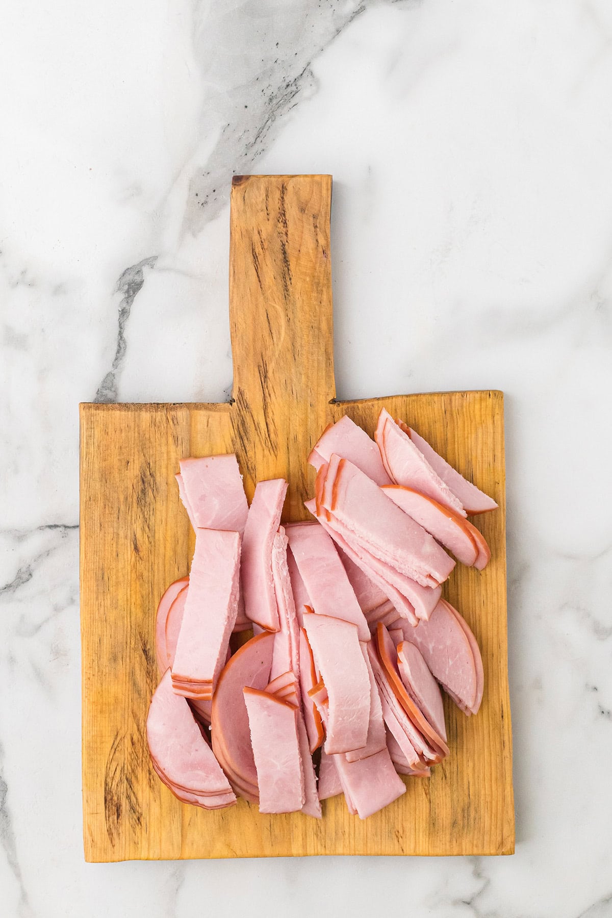 Sliced Canadian bacon on a wooden cutting board, placed on a white marble surface.