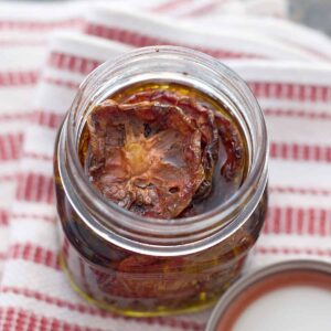 A glass jar filled with roasted tomatoes and olive oil.