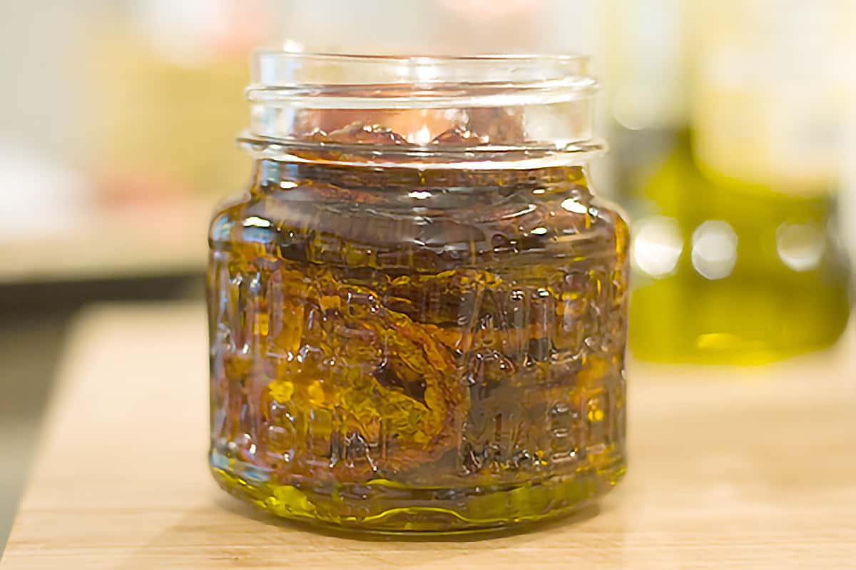Small jar filled with roasted tomato slices and olive oil.