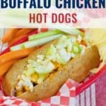 A hot dog bun filled with buffalo chicken, chopped celery, and crumbled blue cheese, served in a red basket with carrot and celery sticks on a checkered paper.