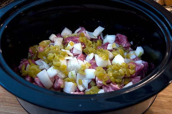 Pork, potatoes, onion, and chilies in a slow cooker.