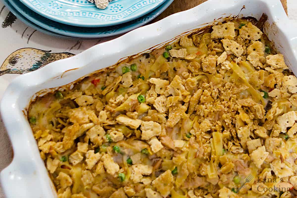 Baked casserole with crispy topping, peas, and noodles in a white dish on a bird-patterned cloth.