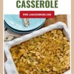 A baked tuna noodle casserole in a white dish, topped with crispy crumbs, beside stacked blue plates.