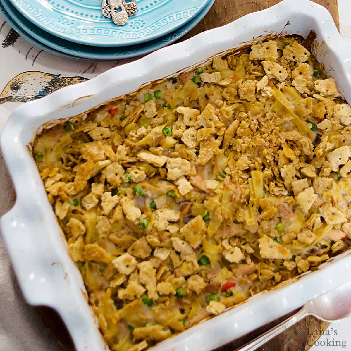 A baked casserole topped with crushed crackers in a white dish, with visible peas and green beans.