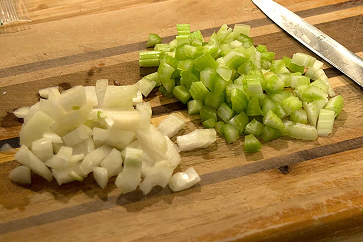 Diced onions and celery on a wooden cutting board with a knife nearby.